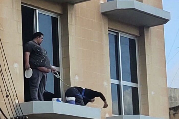 Two men doing dumb things on a balcony, one holding a plate and the other leaning dangerously over the edge.