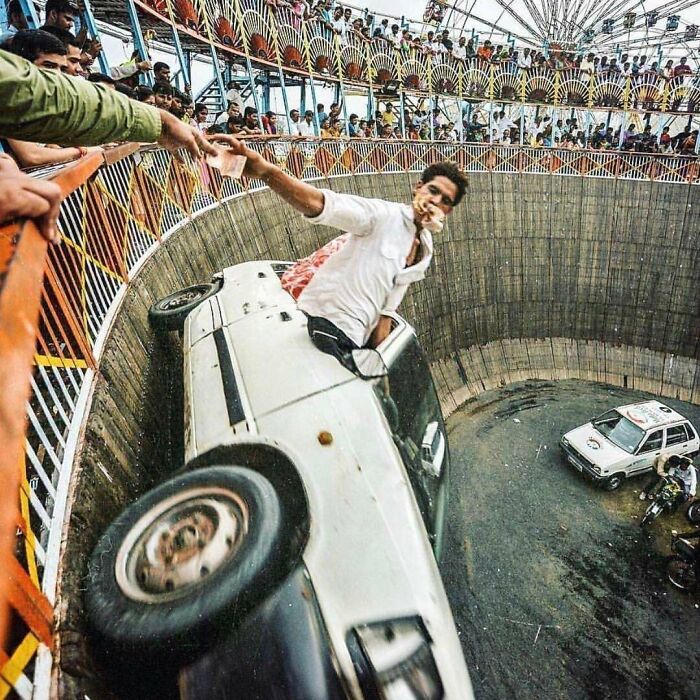 Man performing risky stunt driving inside a circular arena, surrounded by crowds watching dumb things men do explaining why women live longer