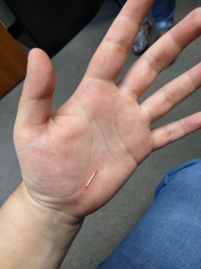 Close-up of a man's hand holding a small metal pin, illustrating men doing dumb things and why women live longer.