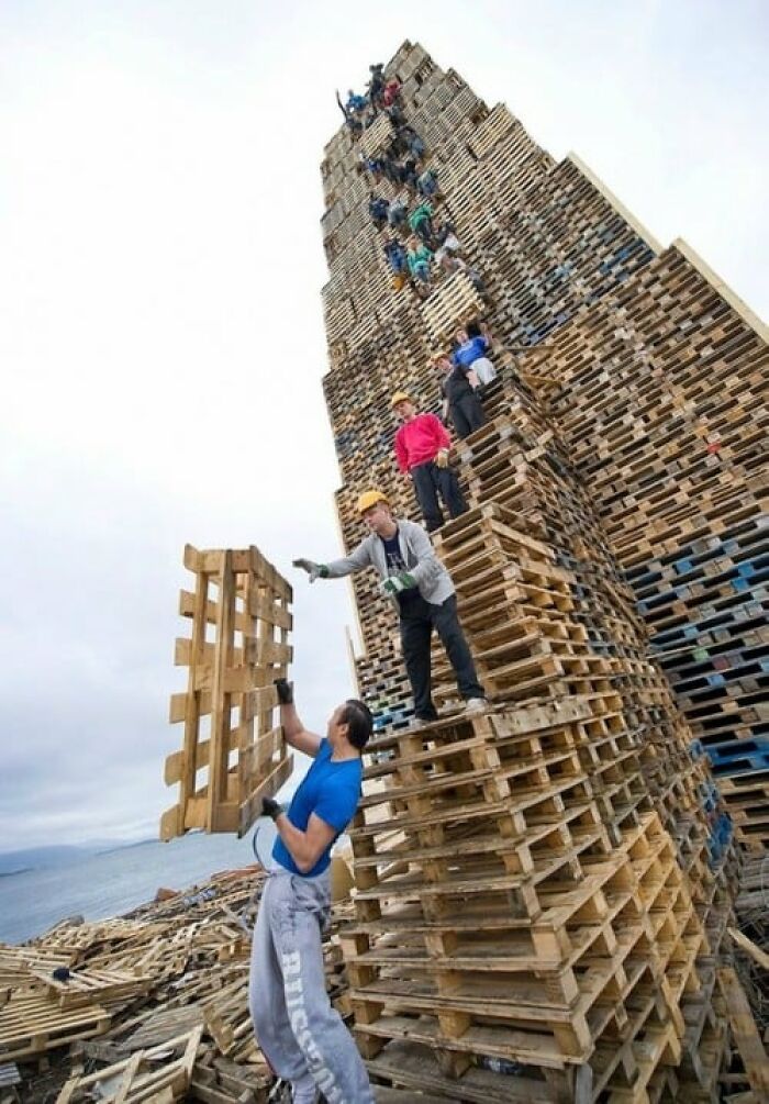 Men stacking wooden pallets dangerously high outdoors, illustrating risky behavior that explains why women live longer.