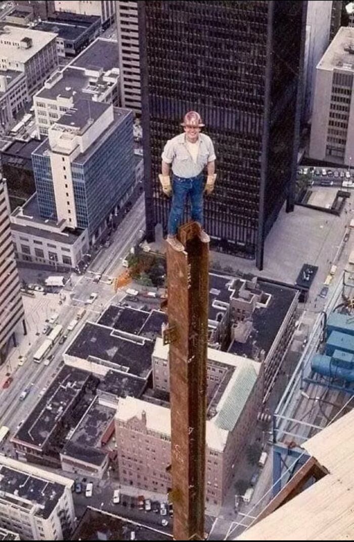 Man wearing construction gear standing atop a tall steel beam high above a city, illustrating men doing dumb things.