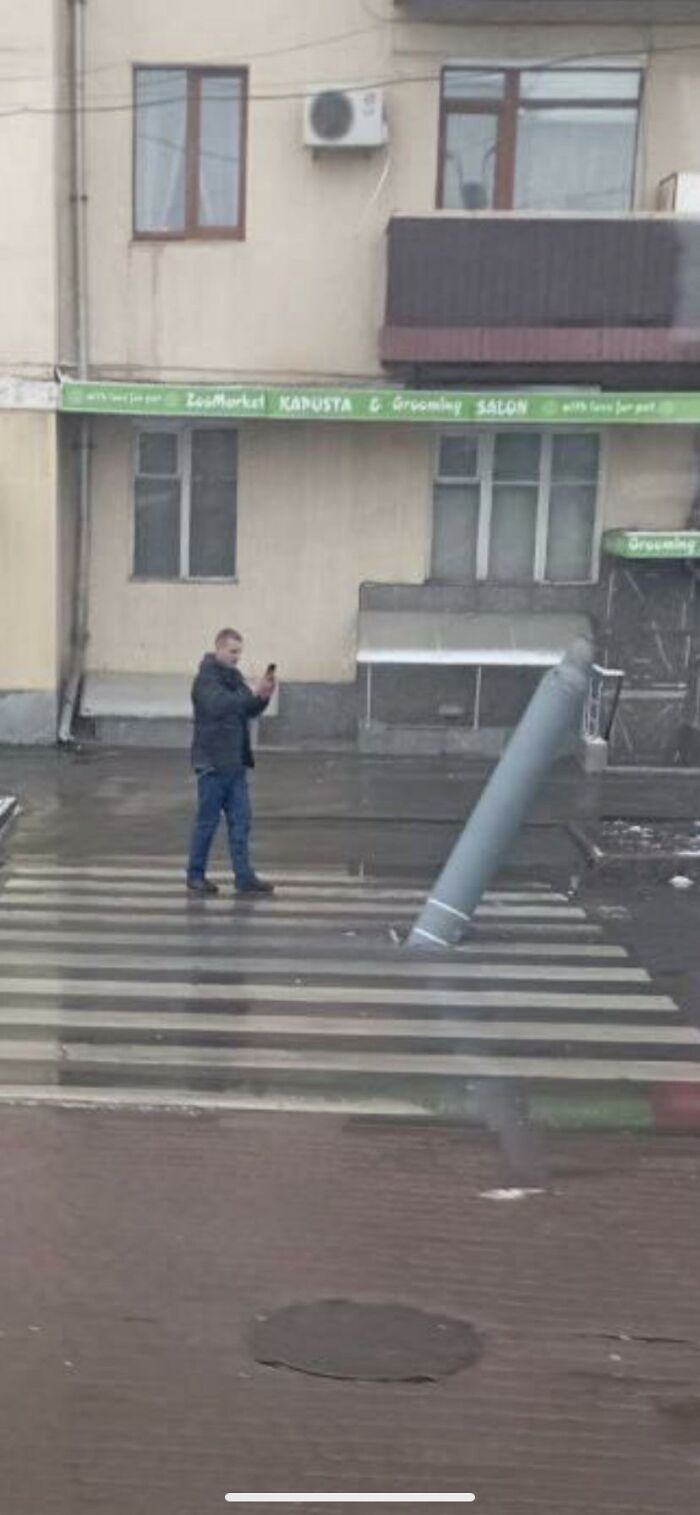 Man doing dumb things taking selfie near fallen streetlight on wet pedestrian crossing in urban area