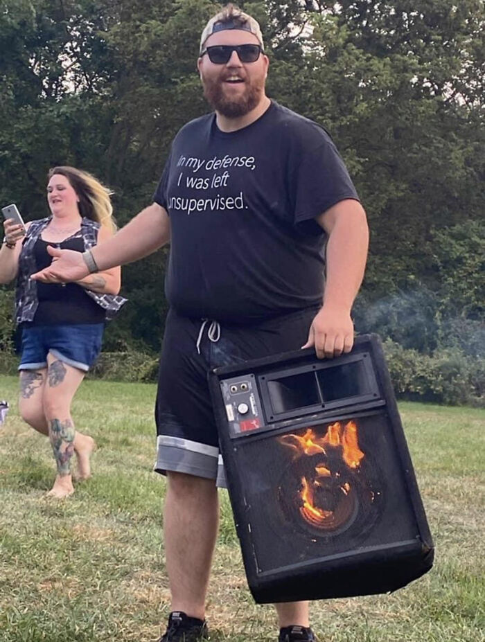Man wearing a black shirt holding a burning speaker outdoors, illustrating men doing dumb things risking safety and longevity.