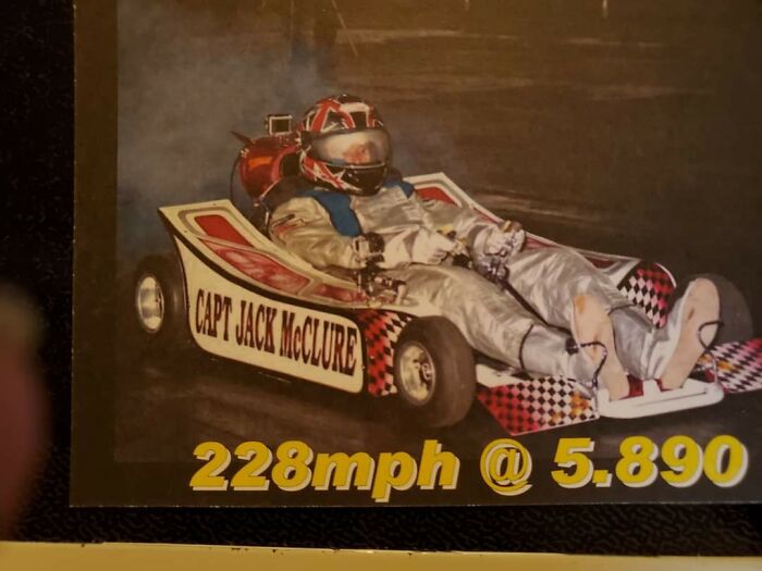 Man in racing suit driving a high-speed go-kart at 228mph, showcasing risky behavior explaining men’s shorter lifespan.