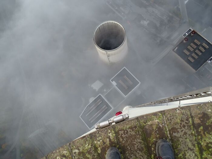 View from height showing man standing near edge above industrial chimney, illustrating men doing dumb things risk theme.