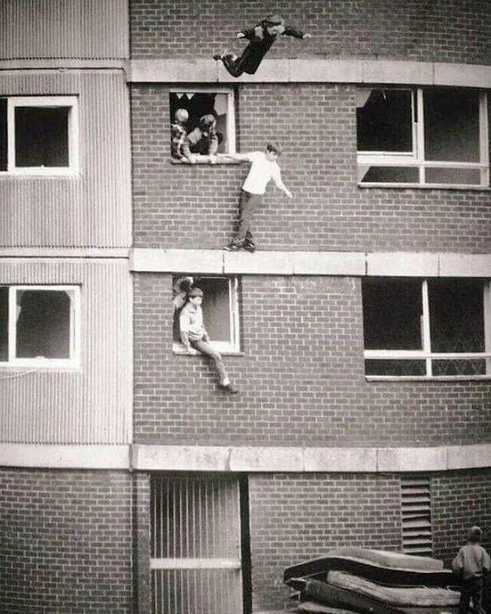 Men doing dumb things by climbing and jumping from a building facade in a risky stunt showing reckless behavior.
