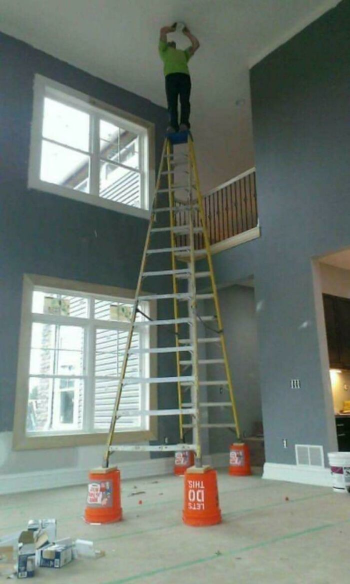 Man doing dumb things standing unsafely on a tall ladder balanced on buckets inside a home under renovation.