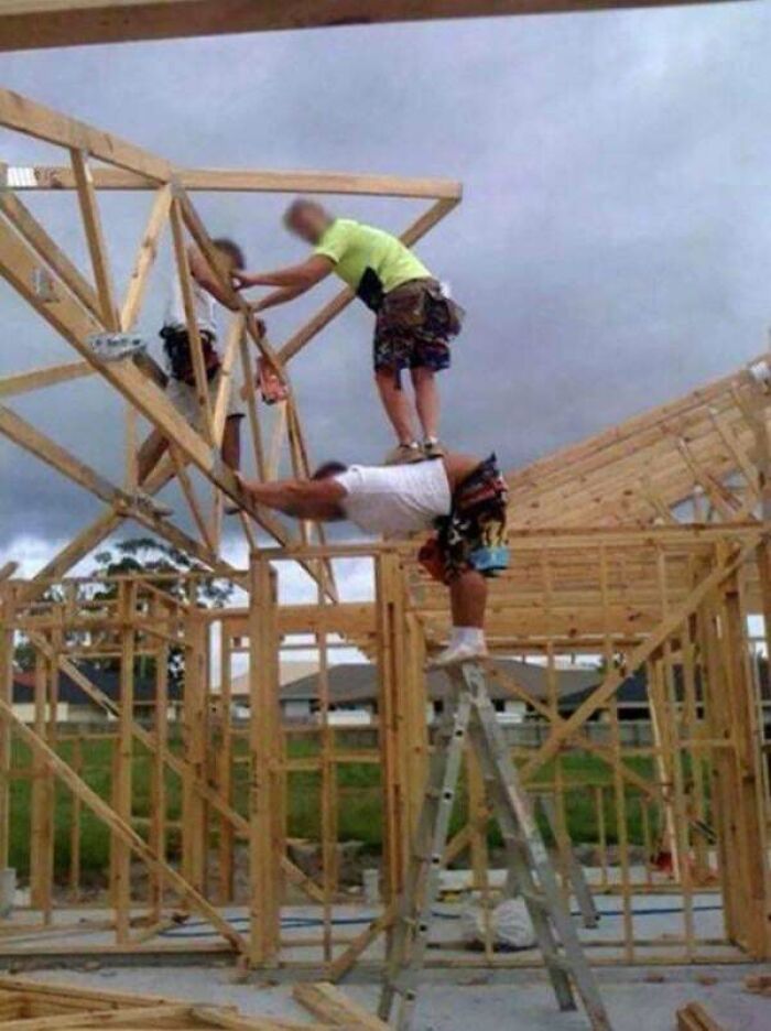 Three men doing dumb things on a wooden frame construction site showing risky behavior and unsafe teamwork.