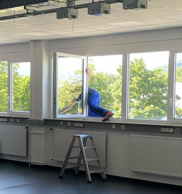 Man climbing through window indoors with ladder nearby illustrating men doing dumb things concept.