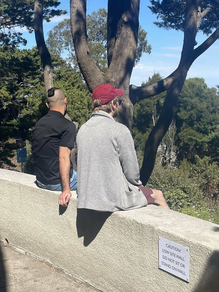 Two men sitting on a low sitewall with a caution sign, an example of men doing dumb things outdoors.