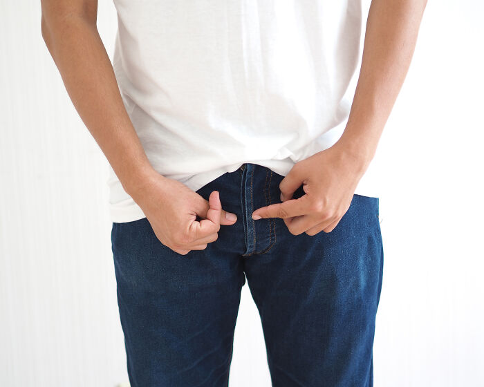 Man in white shirt and jeans unzipping pants, referencing Ozempic side effect of increasing size of men's privates.