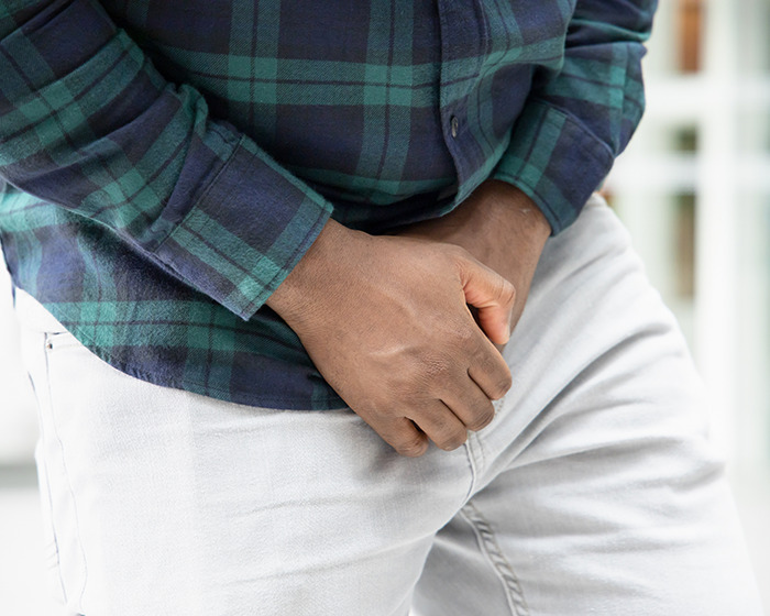 Man in plaid shirt and light pants holding his groin area, illustrating Ozempic side effect on men's privates size.