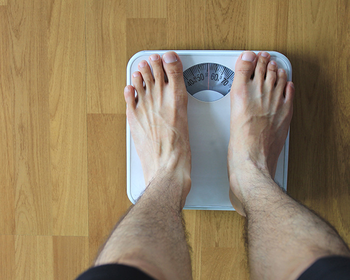 Male feet on a scale measuring weight, conceptually linked to Ozempic and increasing size of men's privates side effect.
