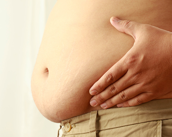 Close-up of a man's hand on his abdomen, illustrating side effects linked to Ozempic and men's private size changes.