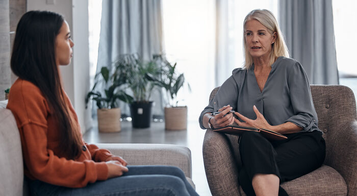 Woman therapist in a modern office listening and taking notes during a counseling session with a young adult client.