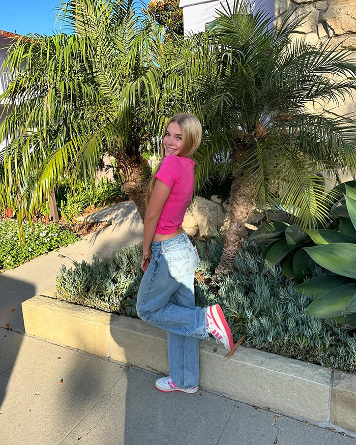 Teen girl, beloved child star from Good Luck Charlie, wearing pink top and jeans, posing outdoors by tropical plants at 16 years old.