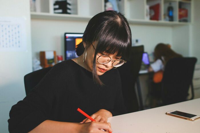 Young woman with glasses writing at a desk, depicting moments people realized their close friend was a total jerk.