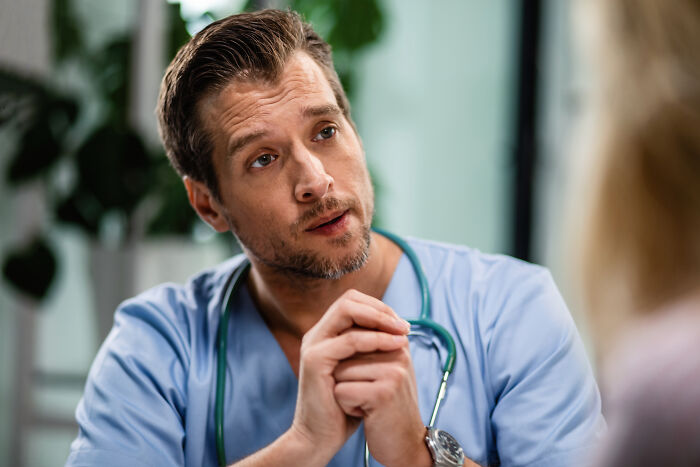 Man in medical scrubs listening intently during a serious conversation about coworker diabolical things to report HR.