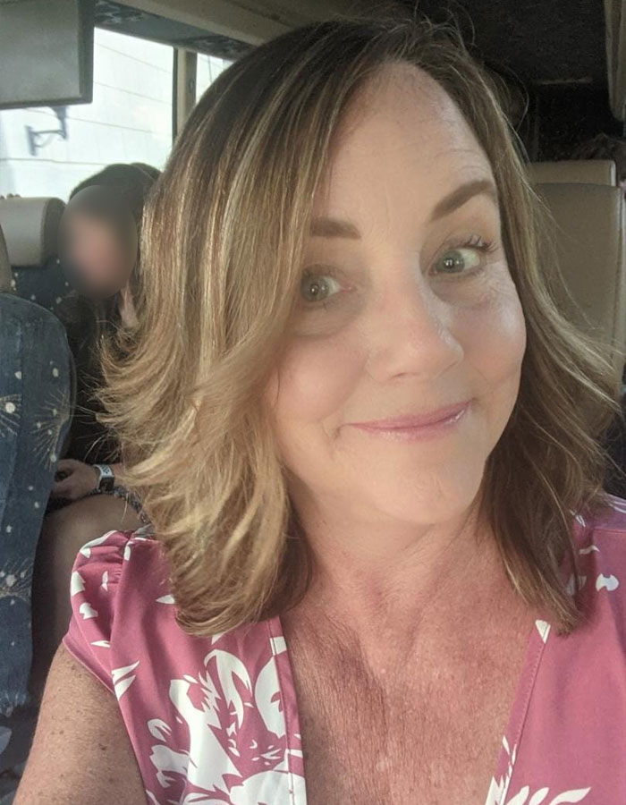 Middle-aged woman smiling on a bus, related to teacher resignation over controversial t-shirt during White House trip.