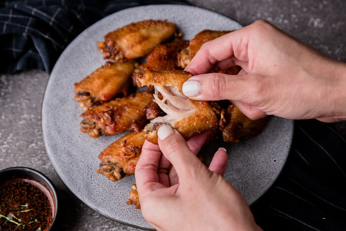 Person peeling crispy chicken wings on a plate, illustrating things non-Americans do like breaking spaghetti.