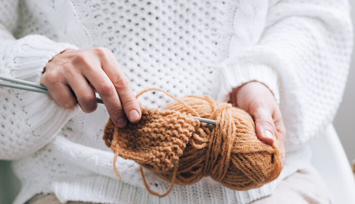 Person knitting brown yarn, showing commitment and focus, illustrating times people committed to a lie way too hard.