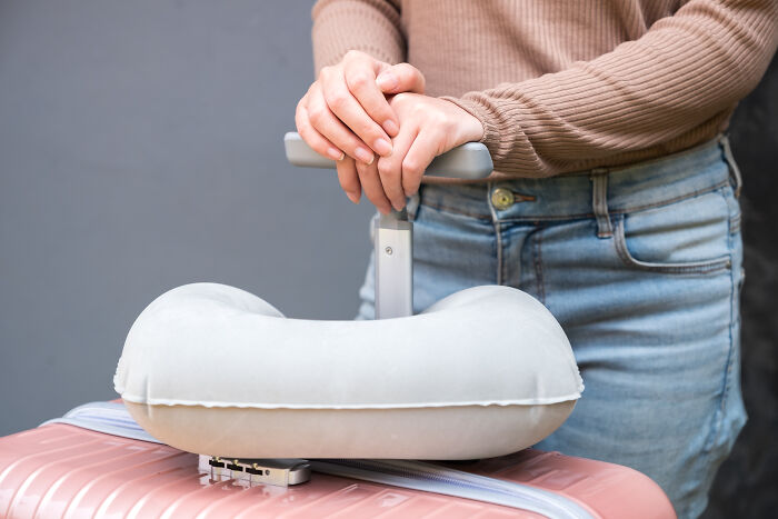 Person holding suitcase handle with travel pillow resting on top, illustrating popular golden travel hacks for comfort and convenience.