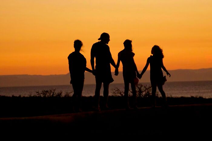 Silhouettes of four people holding hands at sunset, symbolizing casual and harmless looking habits with potential long-term damage.