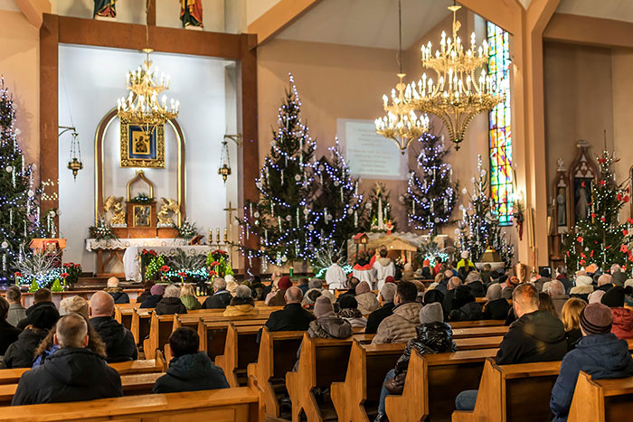 Congregation attending a festive church service decorated with Christmas trees and lights during the holiday season.