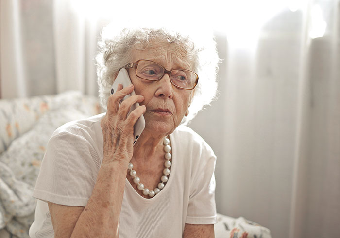 Elderly woman with glasses and pearls making a serious phone call, relating to CPS and forced child tattoo concerns.