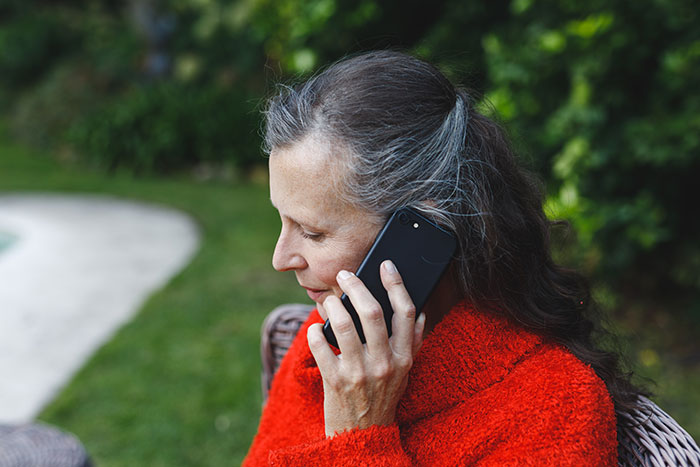 Woman in red sweater outdoors, speaking on phone, representing mother-in-law calling child protective services scenario. Woman in red sweater outdoors, speaking on phone, representing mother-in-law calling child protective services scenario.