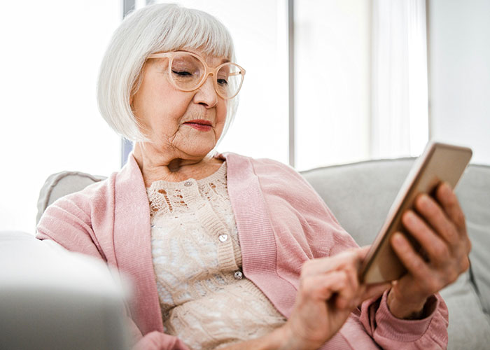 Older woman in pink cardigan using a smartphone, representing mother-in-law&rsquo;s loud comments affecting wedding dress surprise.