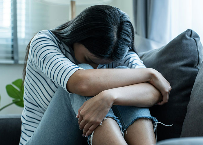 Woman sitting on couch with head down, upset and devastated after mother-in-law&rsquo;s loud comments ruin wedding dress surprise.