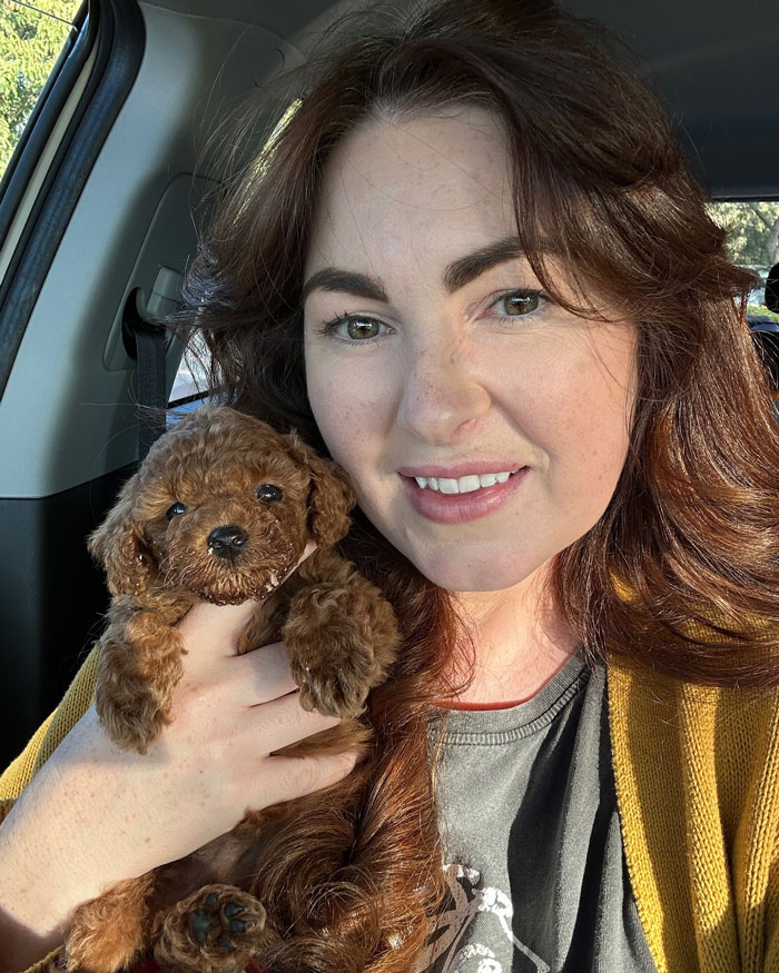 Woman smiling and holding a small curly brown puppy after Aussie vets performed life-saving surgery on the puppy born without butthole.