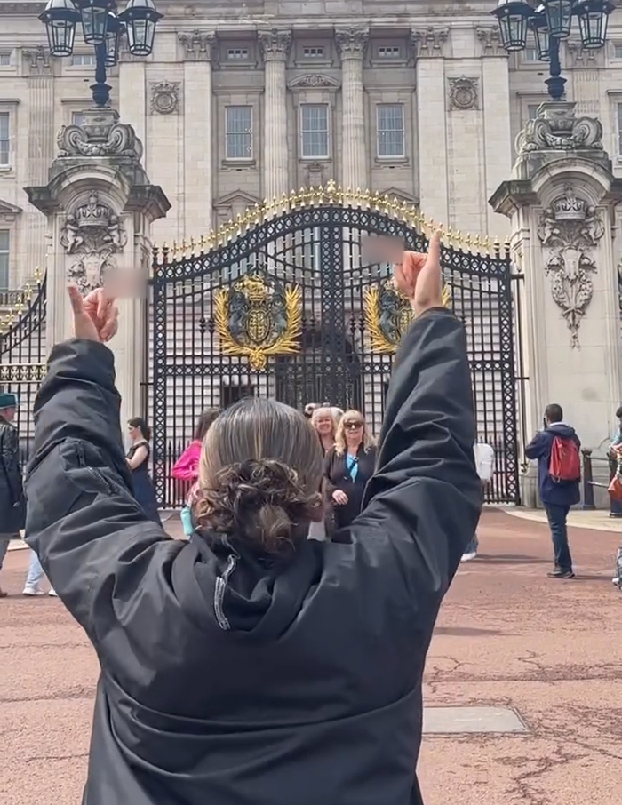 Person with raised middle fingers in front of Buckingham Palace gates, linked to Aboriginal artist breaking King Charles' neck debate. Person with raised middle fingers in front of Buckingham Palace gates, linked to Aboriginal artist breaking King Charles' neck debate.