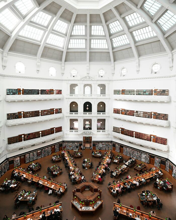 Grandiose library interior with high vaulted ceiling, multiple balconies of books, and people studying at wooden desks.