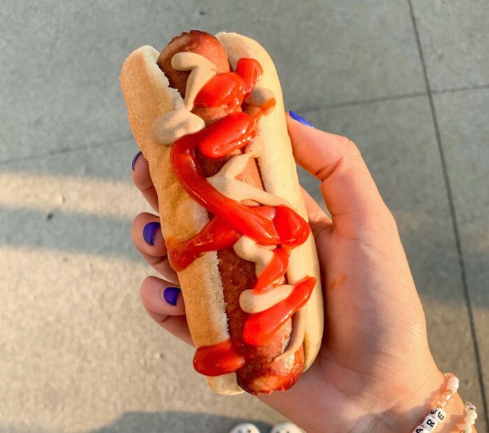 Hand holding a hot dog with mustard and ketchup, illustrating Americans reveal cultural things non-Americans do.