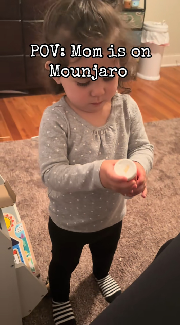 Toddler holding a bottle pretending to inject mom's weight-loss medication on camera in a home setting.
