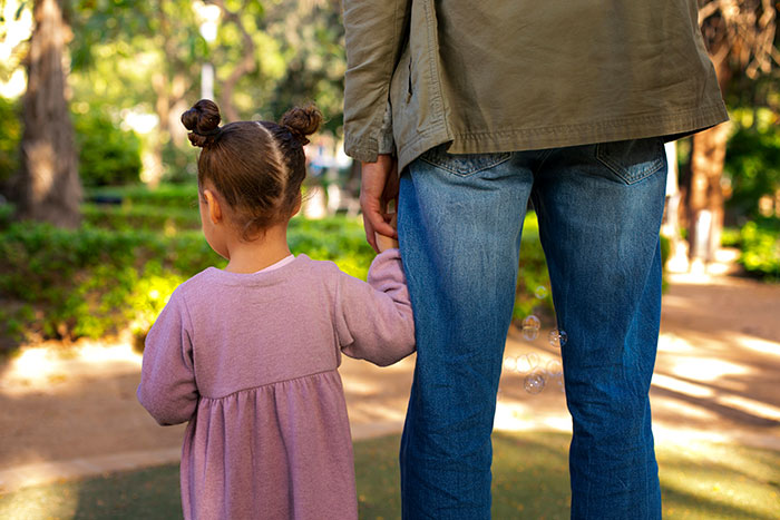 Young girl holding hands with adult in park, illustrating a woman seeking advice on dealing with mom threatening to call CPS. Young girl holding hands with adult in park, illustrating a woman seeking advice on dealing with mom threatening to call CPS.