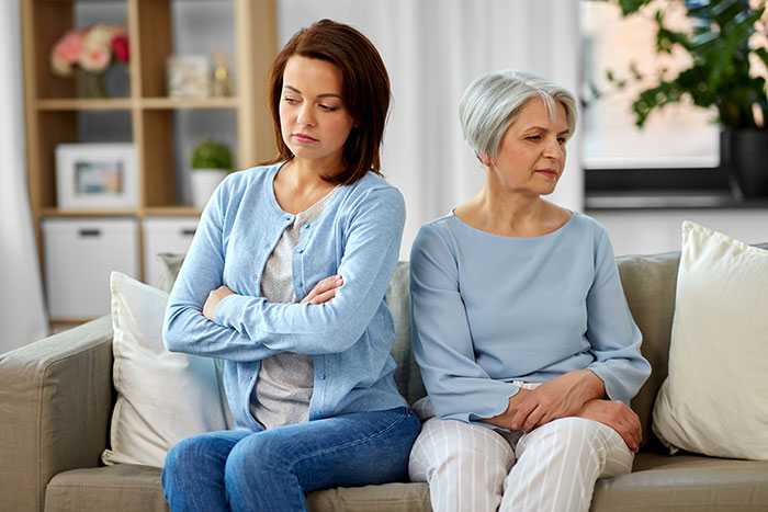 Woman looking angry and upset sitting on couch next to her mother during a tense family conflict about CPS threats. Woman looking angry and upset sitting on couch next to her mother during a tense family conflict about CPS threats.
