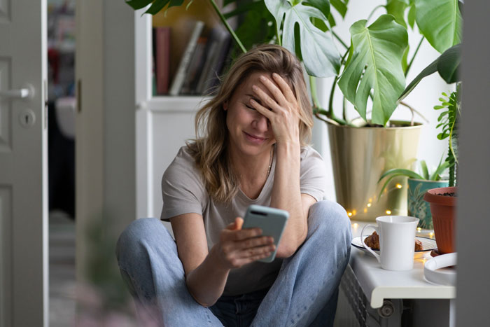 Woman feeling stressed while looking at phone, illustrating bride asking mom not to wear white to wedding conflict. Woman feeling stressed while looking at phone, illustrating bride asking mom not to wear white to wedding conflict.