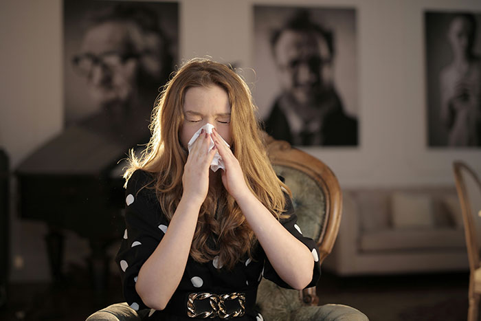 Woman sneezing into tissue indoors, illustrating severe allergy related to cats in a home setting.