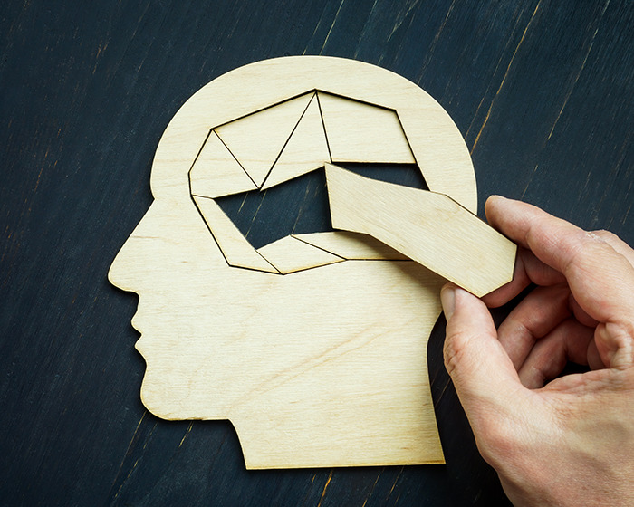 Wooden puzzle of a human head with missing pieces symbolizing early-onset Alzheimer's and memory loss impact.