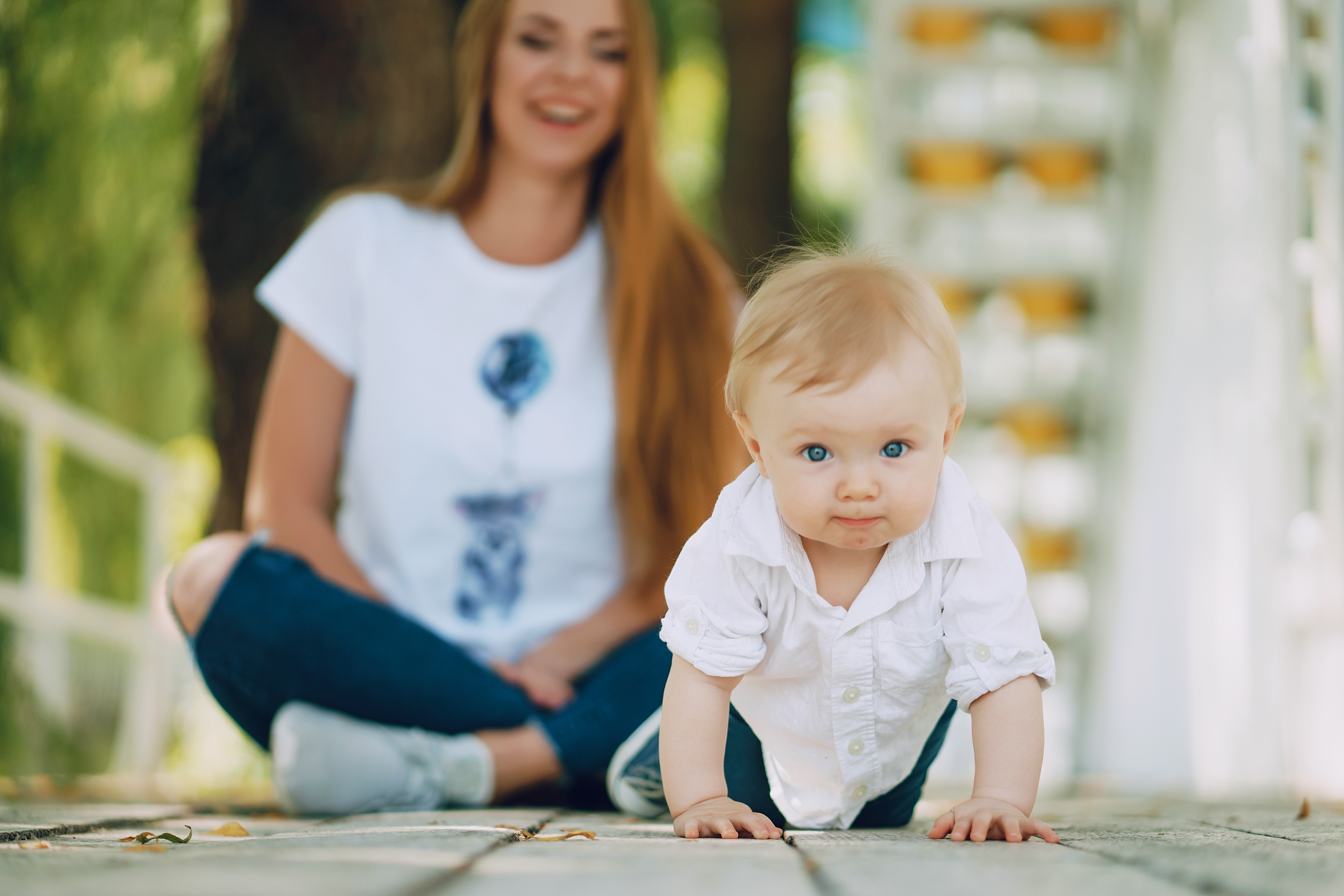 Baby crawling on porch with woman sitting in the background babysitting child during summer outdoors.