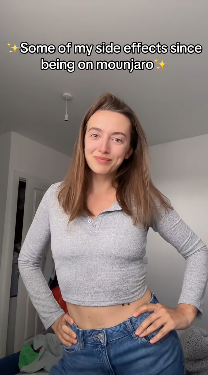 Young woman standing in a casual gray top and jeans sharing her side effects after using Mounjaro for weight loss.