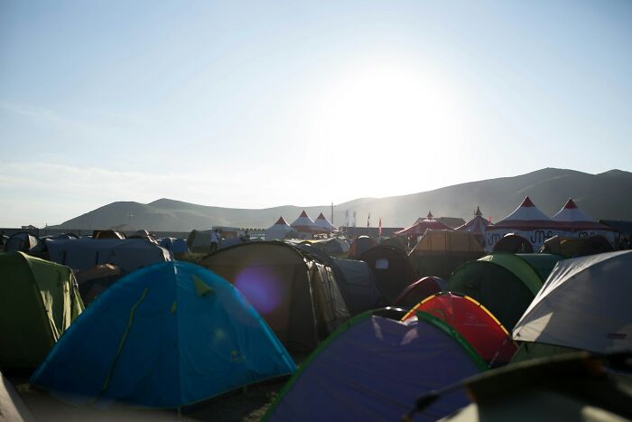 Several tents set up at a campsite in the early morning light with mountains in the background, outdoor gathering scene