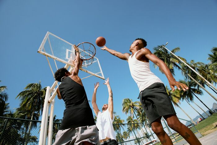 Three men playing outdoor basketball near palm trees under clear sky, unrelated to police nonsense or job questioning.