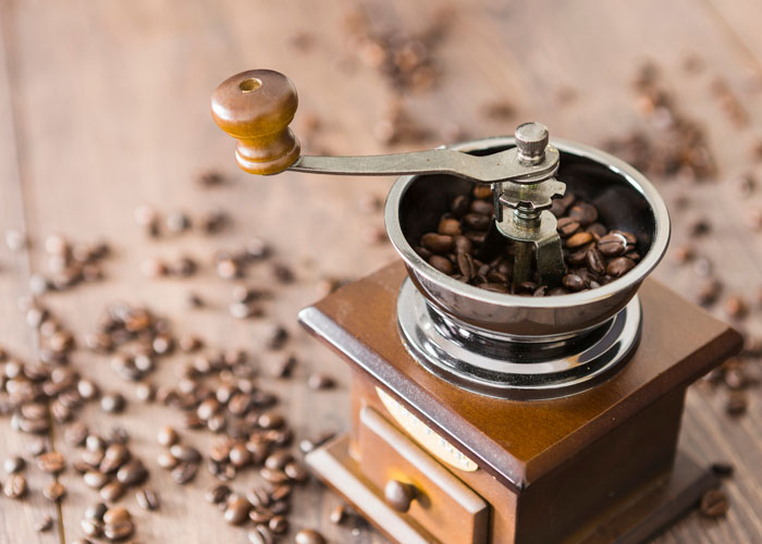Manual coffee grinder filled with beans on wooden surface with scattered coffee beans and neighbor complaint about noisy grinder concept.