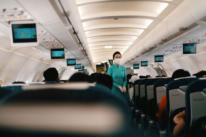 Flight attendant in teal uniform walks down airplane aisle among passengers, while obnoxious guy slaps napping passenger&rsquo;s head incident unfolds.