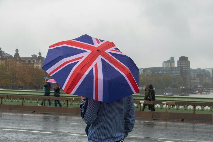 Person holding a Union Jack umbrella on a rainy day, illustrating European netizens correcting country misconceptions.