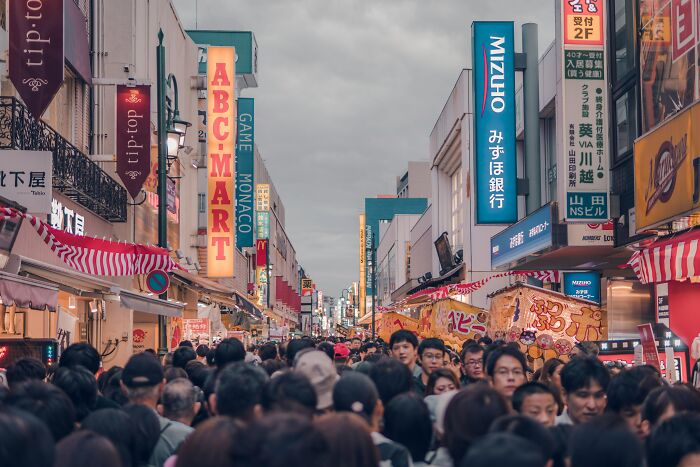 Crowded urban street in Japan with many people and colorful storefront signs illustrating being big in Japan challenges.